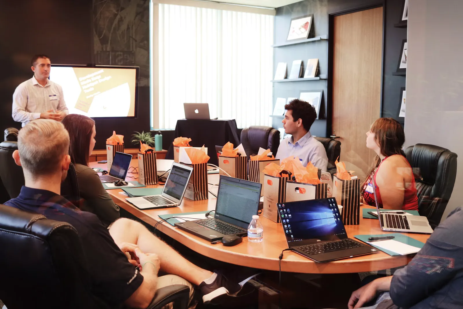 An instructor presenting to a group seated around a conference table with laptops
